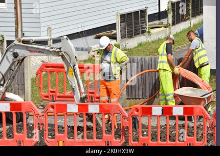 Gruppo di lavoratori che installano bobine di fibra ottica ad alta velocità, cavo per infrastrutture a banda larga in trincea marciapiede al di fuori delle case in via residenziale UK Foto Stock