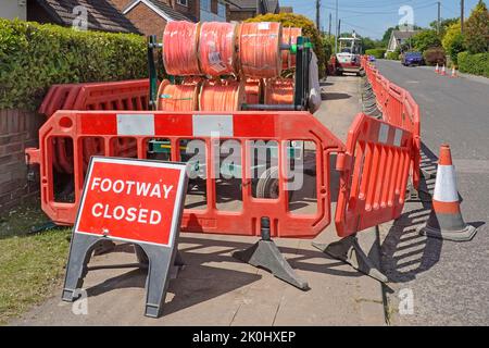 Pedana chiusa segno & alloggiamento pavimentazione chiusa da plastica rossa lavori stradali barriere di sicurezza fibra veloce a banda larga cavi tamburi mini scavatore lavoro Inghilterra UK Foto Stock