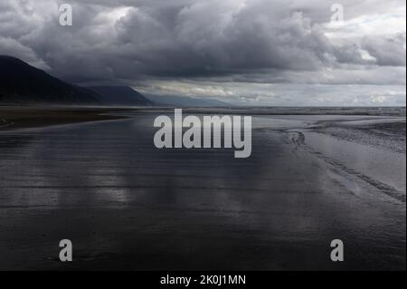 Nuvole tempestose si riflettevano su una spiaggia bagnata Foto Stock