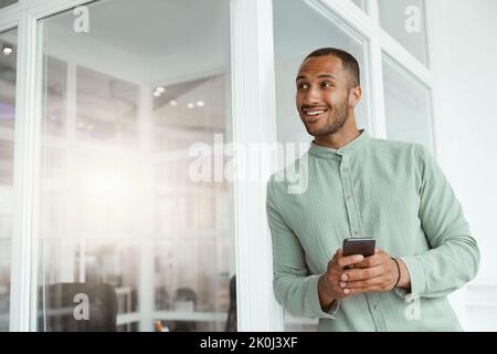 Uomo d'affari africano sorridente in piedi in ufficio moderno e tenendo il telefono Foto Stock