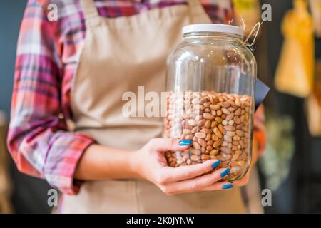 Donna lavora nel negozio di frutta e verdura. Lei tiene il vaso con la mandorla. Foto Stock