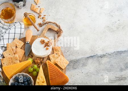 Assortimento di formaggi, miele, cracker, mirtilli, uva con vino rosso e bianco in bicchieri antipasto server su tavola di marmo bianco su fondo grigio Foto Stock