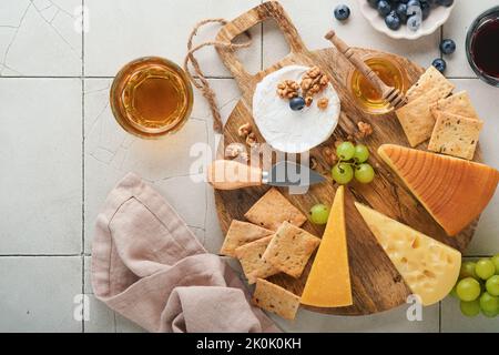 Assortimento di formaggi, miele, cracker, mirtilli, uva con vino rosso e bianco in bicchieri antipasto server su tavola di marmo bianco su fondo grigio Foto Stock