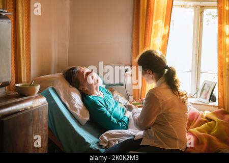 Infermiera che allatta la donna anziana paralizzata con purea attraverso il tubo e la siringa mentre si prende cura del paziente a casa Foto Stock