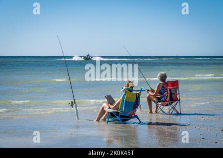 Sarasota, FL, US-23 novembre 2020: Due donne che pescano sulla spiaggia tropicale con motoscafo sullo sfondo. Foto Stock