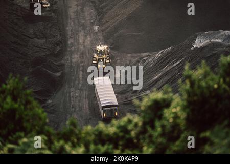 Vista aerea della pala caricatrice moderna che trasporta merci lungo le giacenze di carbone durante la luce del giorno Foto Stock