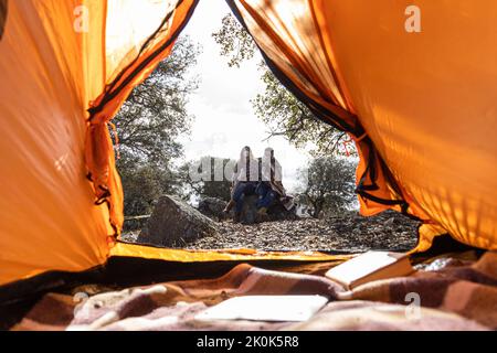 Giovane coppia in campeggio seduto vicino tenda avvolto su coperta accogliente mentre si beve una bevanda calda Foto Stock