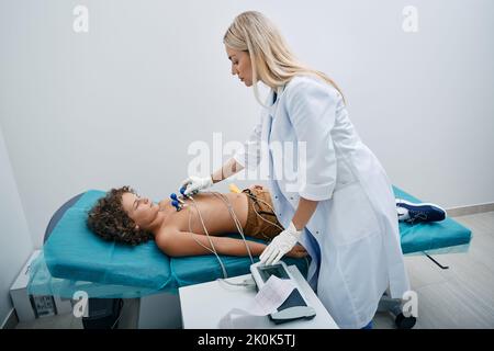 Cardiologo che installa i sensori del vuoto sul torace del bambino maschio durante la procedura di elettrocardiogramma presso la clinica medica. ECG per bambini Foto Stock