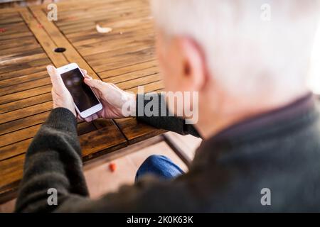 Uomo anziano che usa il suo smartphone seduto al tavolo di casa Foto Stock