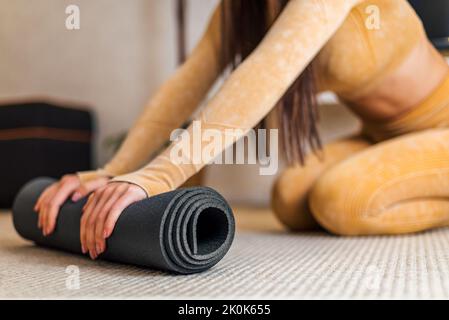 Immagine di energica giovane bruna donna, con tuta gialla, con il suo tappetino nero per lo yoga. Foto Stock