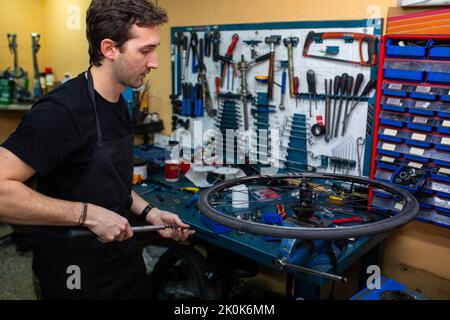 Giovane uomo in grembiule che pompa aria nel pneumatico di bicicletta mentre lavora in officina professionale Foto Stock