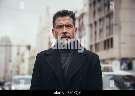 Uomo di mezza età, sicuro e attento, che guarda la fotocamera mentre si trova in una strada urbana Foto Stock