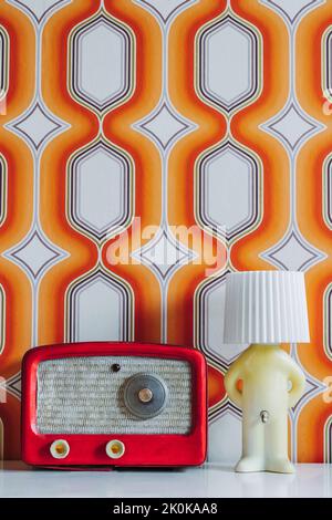 Set di radio rossa e lampada a forma di ragazzo posto sul tavolo contro pareti colorate con forme geometriche Foto Stock