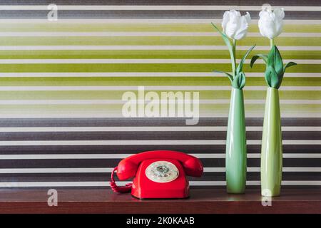 Tulipani bianchi in vasi verdi posti vicino retro telefono rosso su tavolo di legno contro parete colorata Foto Stock