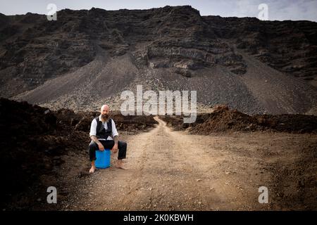 L'uomo con vestito è seduto completamente disperato e bussato fuori su un canister blu da qualche parte in nessun posto nel deserto vulcanico alla fine o Foto Stock