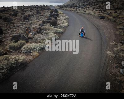 L'uomo con vestito è seduto completamente disperato e bussato fuori su un canister blu da qualche parte in nessun posto nel deserto vulcanico alla fine o Foto Stock