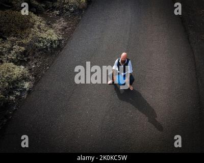 L'uomo con vestito è seduto completamente disperato e bussato fuori su un canister blu da qualche parte in nessun posto nel deserto vulcanico alla fine o Foto Stock