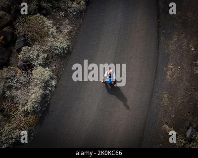 L'uomo con vestito è seduto completamente disperato e bussato fuori su un canister blu da qualche parte in nessun posto nel deserto vulcanico alla fine o Foto Stock