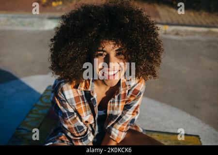 Content hipster afro-americano femminile in camicia a scacchi e con acconciatura afro godendo il tramonto e guardando la macchina fotografica Foto Stock