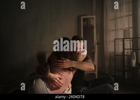 Coppia di adulti di media età seduta a letto di notte e abbracciata. Foto Stock