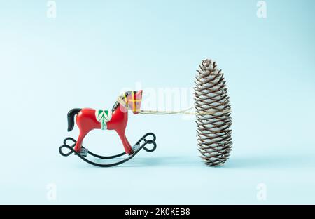 Retrò Natale a dondolo ornamento cavallo legato a un cono di pino bianco su uno sfondo azzurro. Concetto minimo. Foto Stock