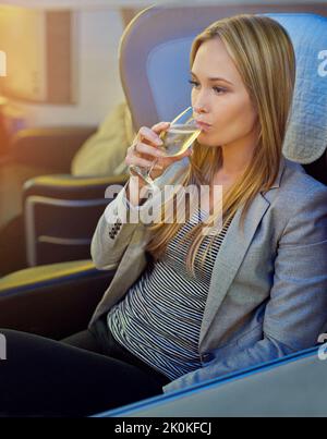 È l'unico modo per volare: Una giovane donna che beve champagne in prima classe su un aereo. Foto Stock