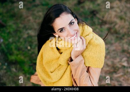 Da sopra ritratto di donna allegra ed elegante con vestito giallo in piedi su erba e guardando la macchina fotografica Foto Stock