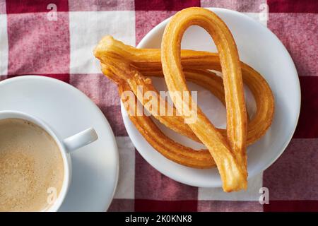Churros appetitosi sul piatto e tazza di caffè fresco del mattino servito sul tovagliolo sul tavolo per la colazione in cucina Foto Stock