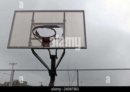 Un canestro da basket fatiscente senza rete e uno schienale rotto si trovano trascurati in un parco giochi. Foto Stock