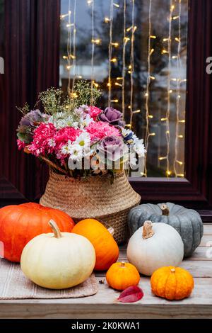 Casa decorata per vacanze autunnali. Porta illuminata con ghirlanda e portico con varie zucche e fiori nel cesto di vimini per il giorno del Ringraziamento o Foto Stock