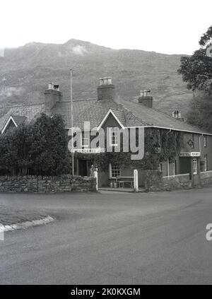 1956, storico, un gentiluomo che si trova fuori dall'entrata del Pen-y-Gwryd Hotel, Nant Gwynant, Caernarfon, Galles, Regno Unito. Situato in una valle in Snowdonia, fu un casale in pietra quando fu costruito nel 1810 e in seguito divenne una locanda per escursionisti e arrampicatori in visita a Snowdonia. Nel 1953, fu la base di addestramento di Sir Edmund Hillary prima della sua salita al Monte Everest. Foto Stock