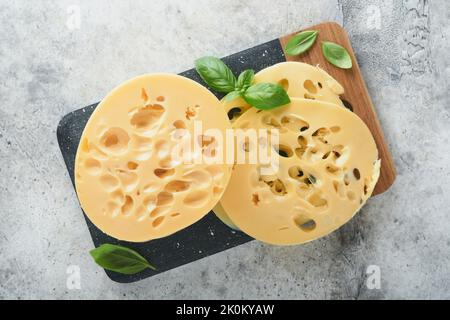 Formaggio Maasdam o Radamer. Pezzo di formaggio su marmo nero o stalla di pietra su vecchio sfondo grigio cemento. Vista dall'alto. Spazio libero per il testo. Foto Stock