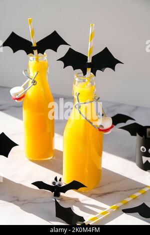 Halloween mocktail. Cocktail analcolico all'arancia per la festa di Halloween su un tavolo bianco. Le cannucce sono decorate con pipistrelli di carta tagliati. Halloweens spooky Foto Stock