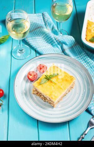 Deliziose lasagne italiane fatte in casa con salsa al bachamel e bicchieri di vino su sfondo di legno blu Foto Stock