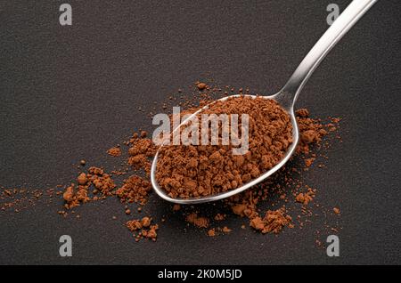 Polvere di cacao in cucchiaio su fondo nero Foto Stock