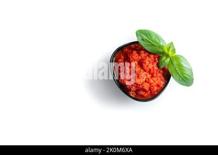 Ajvar in una fiala nera con basilico su fondo bianco. Isolare. Pasta di peperone dolce Foto Stock