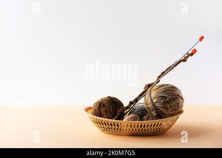 Palle di filo beige e marrone in un cesto beige con aghi per la lavorazione a maglia di abiti caldi, hobby per la lavorazione a maglia Foto Stock