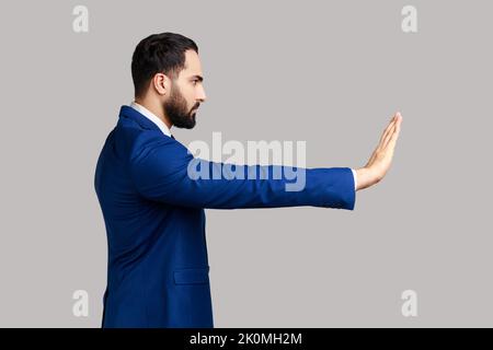 Vista laterale di un uomo serio sopportato che fa un gesto di arresto mostrando palmo di mano, divieto di conflitto avvertimento circa pericolo, smettere di bullismo, indossare tuta. Studio in interni isolato su sfondo grigio. Foto Stock