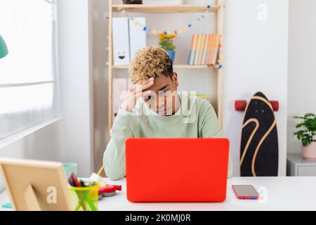 Ragazzo stressato seduto alla scrivania che studia sul computer portatile in camera Foto Stock