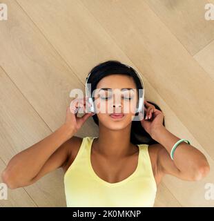 Entrare in modalità relax con musica rilassante. Ripresa ad alto angolo di una giovane donna che ascolta musica sdraiata su un pavimento in legno. Foto Stock