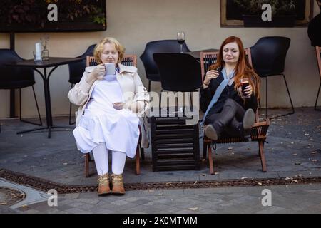 Due donne insieme - bionde in luce e rosso in abiti scuri che parlano al bar di un caffè di strada. Foto Stock