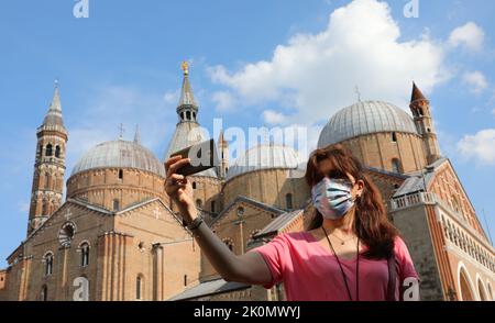 Giovane donna con maschera chirurgica scattando una foto con smartphone a Padova e alla Basilica di Sant'Antonio in Italia Foto Stock