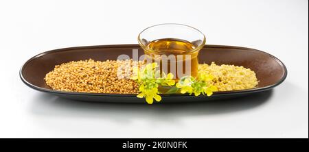semi di senape, olio, schiacciate e fiori su fondo bianco. utile in cucina e cura del corpo esterno. Semi di senape e piante di senape con baccelli e fiori Foto Stock