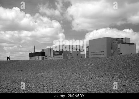 Immagine monocromatica di due persone che camminano accanto alla centrale nucleare di Dungeness, Kent, Inghilterra. Foto Stock