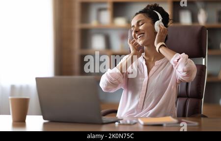 Giovane donna allegra che ascolta musica in ufficio Foto Stock
