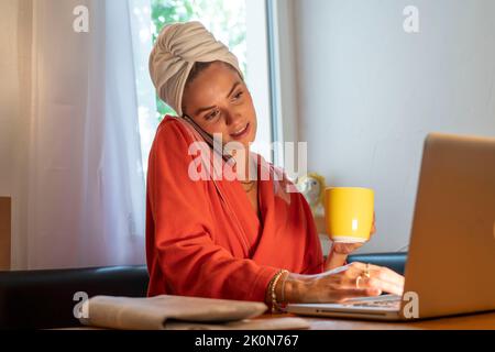 Immagine simbolica Precrastinazione, giovane donna cerca di fare molte cose allo stesso tempo, dopo il bagno, sul computer, telefono, giornale, e colazione Foto Stock