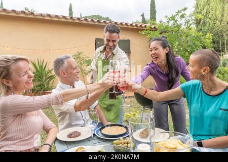 Gli uomini e le donne di mezza età felici allietano al picnic della casa di campagna. Concetto di stile di vita con amici allegri divertirsi insieme nel pomeriggio rilassante Foto Stock