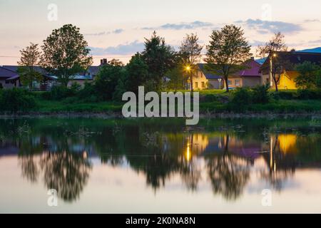 Vista del villaggio di Krpelany che riflette nel canale del fiume Vah. Foto Stock
