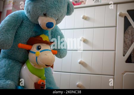 orsacchiotto in sella a un cavallo giocattolo nella stanza dei bambini Foto Stock