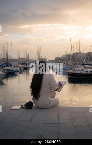 Donna sulla schiena che lavorava seduto con vista su un porto Foto Stock
